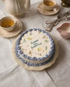 a birthday cake sitting on top of a table next to tea cups and saucers