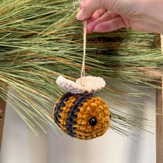 a hand is holding a crocheted ornament hanging from a pine tree