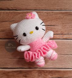 a crocheted hello kitty doll is posed on a wooden surface with wood planks