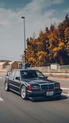 a black car driving down the road with trees in the background