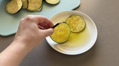 someone cutting up some zucchini on a plate with oil in the bowl next to it