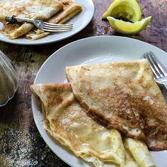 two white plates topped with pancakes next to lemon wedges