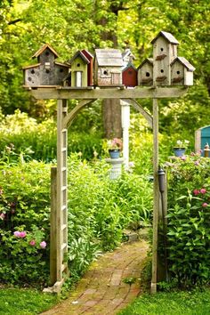 a garden with lots of bird houses on top of the wooden structure in front of flowers and trees