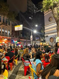 many people are sitting at tables and chairs outside in the evening with lights shining on them