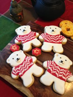 decorated cookies with teddy bears on a wooden cutting board next to other decorations and gold coins