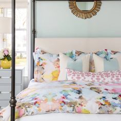 a white bed topped with lots of pillows next to a dresser and mirror in a bedroom