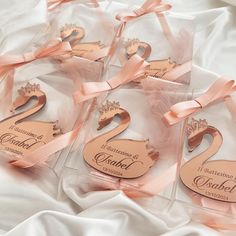 six wedding favors in clear boxes with pink ribbons and bows on white satin fabric background