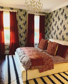 a large bed sitting in the middle of a bedroom next to two windows with red curtains