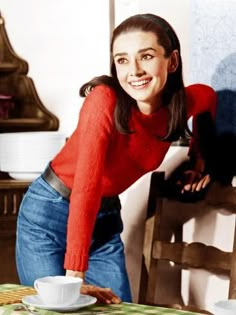 a woman leaning over a table with a cup and saucer on it