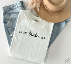 two t - shirts with the words in my bride era on them next to a hat