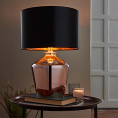 a table with a lamp on top of it next to a book and glass candle