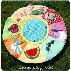 a circular play mat with various items on it in the grass, including an insect and watermelon design