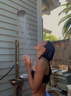 a woman standing in front of a house drinking out of a water faucet