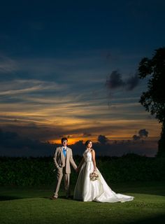 a bride and groom standing in the grass at sunset