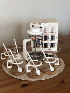 a coffee maker sitting on top of a wooden table next to cups and spoons