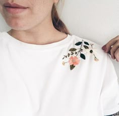 a close up of a person wearing a white shirt with flowers and leaves on it