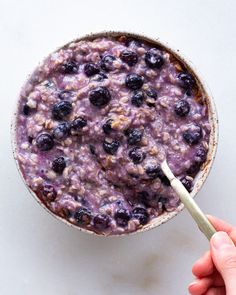 a bowl of oatmeal with blueberries in it and a hand holding a spoon