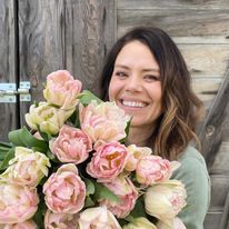 a woman holding a bouquet of flowers in front of a wooden door smiling at the camera