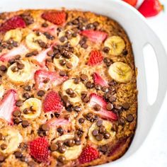 a white casserole dish filled with fruit and nutritious toppings next to two strawberries