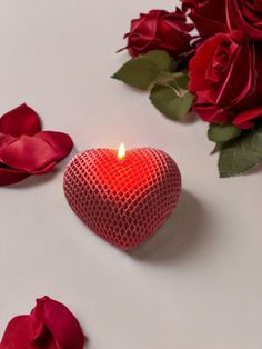 a heart shaped candle sitting next to red roses