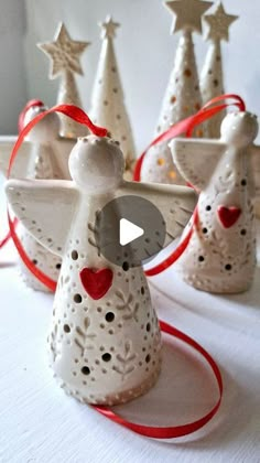 three white ceramic angel ornaments with red ribbons and bows on them, sitting next to each other