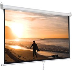 a man walking on the beach at sunset in front of a large screen tv that is hanging from a wall