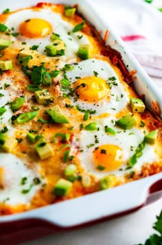 an egg dish in a red casserole dish with green onions and cheese on top