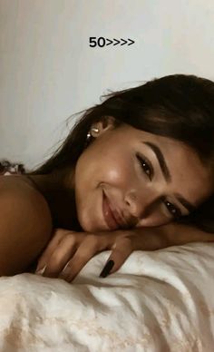 a beautiful young woman laying on top of a bed next to a white wall and smiling at the camera