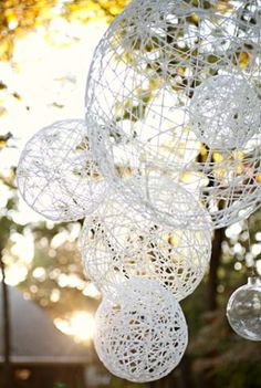 some white balls hanging from the ceiling in front of trees and sunlight shining on them