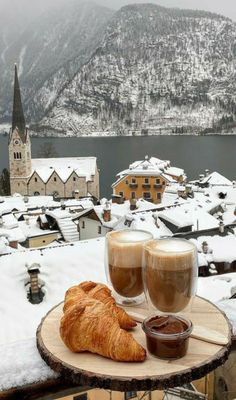 two glasses of coffee and croissants on a table with snow covered mountains in the background