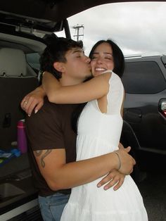 two people hugging each other in front of a car