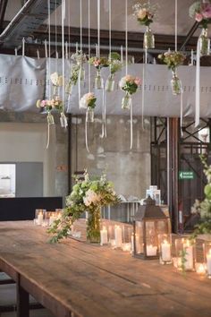 a wooden table topped with lots of vases filled with flowers and greenery hanging from the ceiling