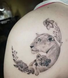 a woman with a lion and cub tattoo on her back shoulder is holding flowers in front of her arm