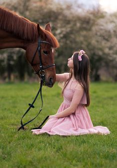 a girl in a pink dress petting a brown horse