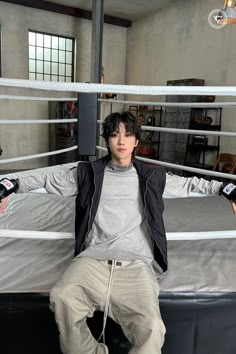 a young man sitting on top of a bed in a room with two boxing ropes