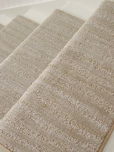 three beige rugs on the floor in front of a white wall and window sill