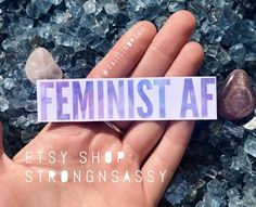 a hand holding a sticker with the word feminist af on it next to some rocks