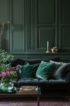 a living room with green walls and black couches in the center, surrounded by greenery