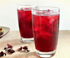 two glasses filled with red liquid sitting on top of a wooden table next to a plate