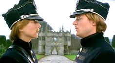 two men in uniform standing next to each other near a building with a castle behind them