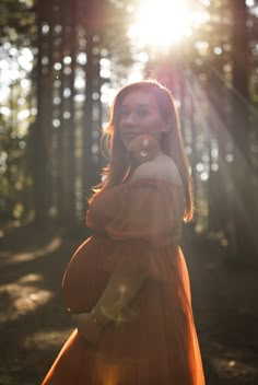 a woman in an orange dress is standing in the woods with her hands on her hips