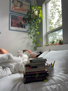 a stack of books sitting on top of a bed next to a potted plant