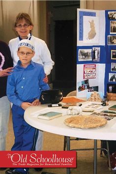 three people standing around a table with various items on it and an old schoolhouse sign in the background