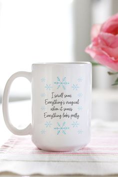 a white coffee mug sitting on top of a table next to a pink flower in a vase