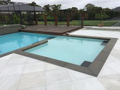 an empty swimming pool in the middle of a backyard with concrete pavers and wooden decking