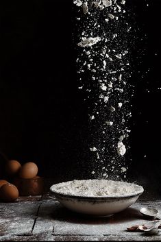 flour is falling into a bowl with eggs in the background