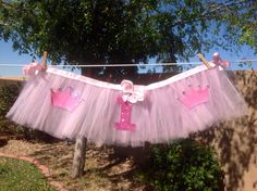 a pink tutu skirt hanging on a clothes line with two little princess crowns attached to it