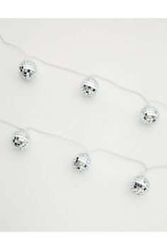 several silver balls are hanging from a string on a white wall with lights attached to it