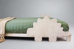 a wooden dinosaur bed sitting next to a green bedspread on a gray background