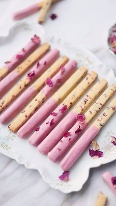 pink and yellow popsicles on a white plate with rose petals scattered around them,